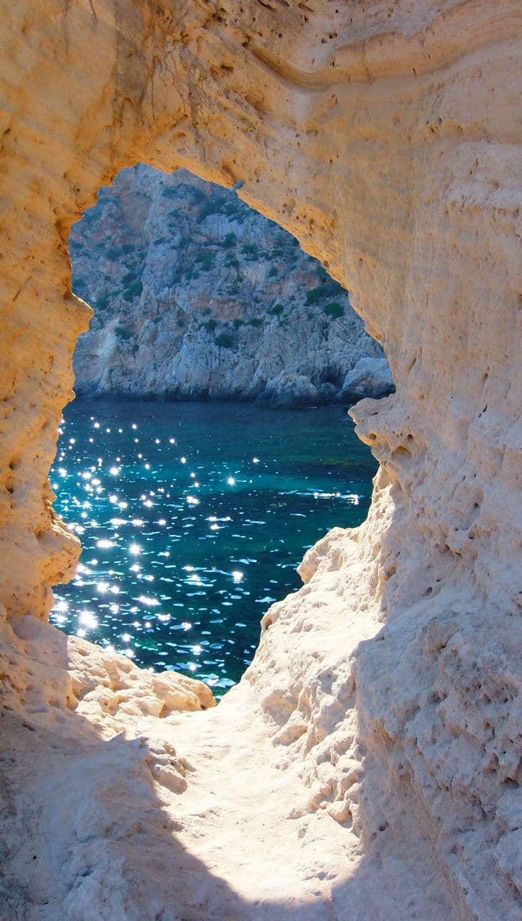 Sunlit cave passage opening onto a shimmering turquoise sea